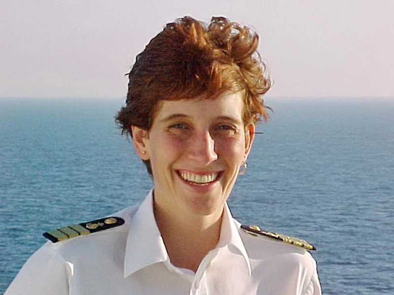 Smiling officer in white uniform against the backdrop of the vast, blue ocean.