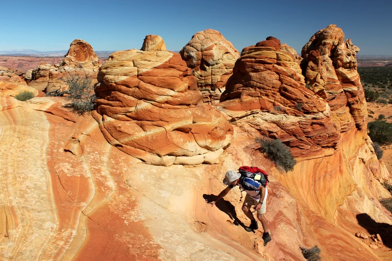 Wanderer erklimmt die markanten, rötlich geschichteten Felsformationen der Coyote Buttes South in den Vermillion Cliffs