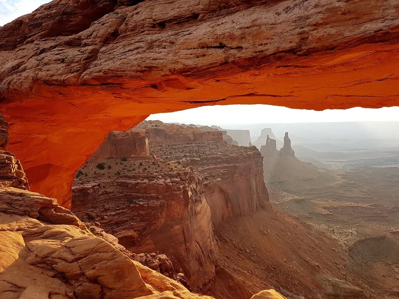 Blick durch den Mesa Arch auf die weite Canyonlandschaft des Canyonland Nationalparks im Morgenlicht.