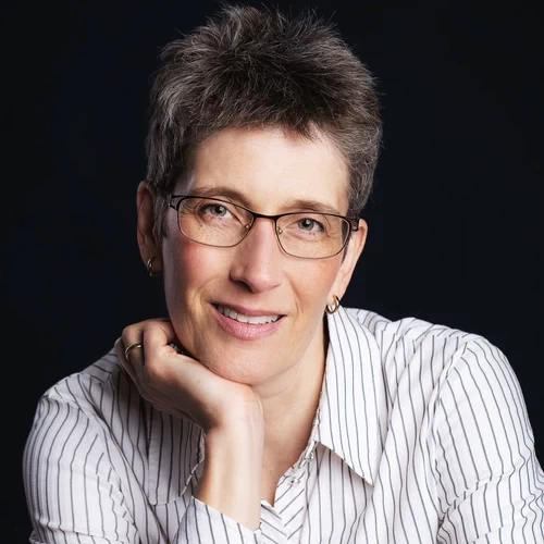 Porträt von Sabine Schroeder, Autorin, mit Kurzhaarschnitt und Brille vor dunklem Hintergrund (Nahaufnahme)